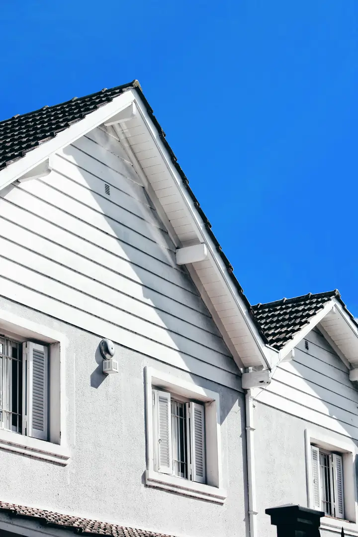 Woning met een donker hellend dak en witte gevelbekleding, omgeven door groen en rozenstruiken.