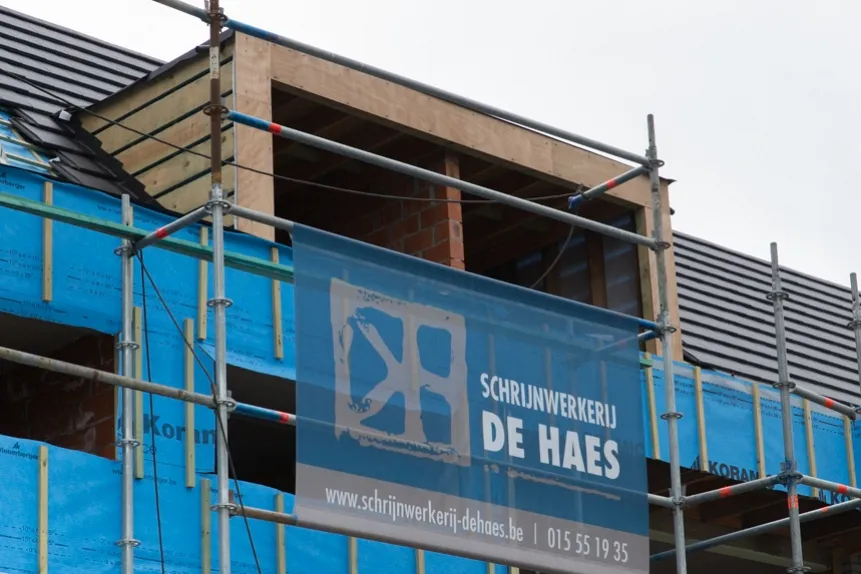 Dakwerken De Haes plaatst daktimmer en gevelbekleding op een woning in Waarloos, Kerkelei: werf met steigers en blauwe werfbanner.